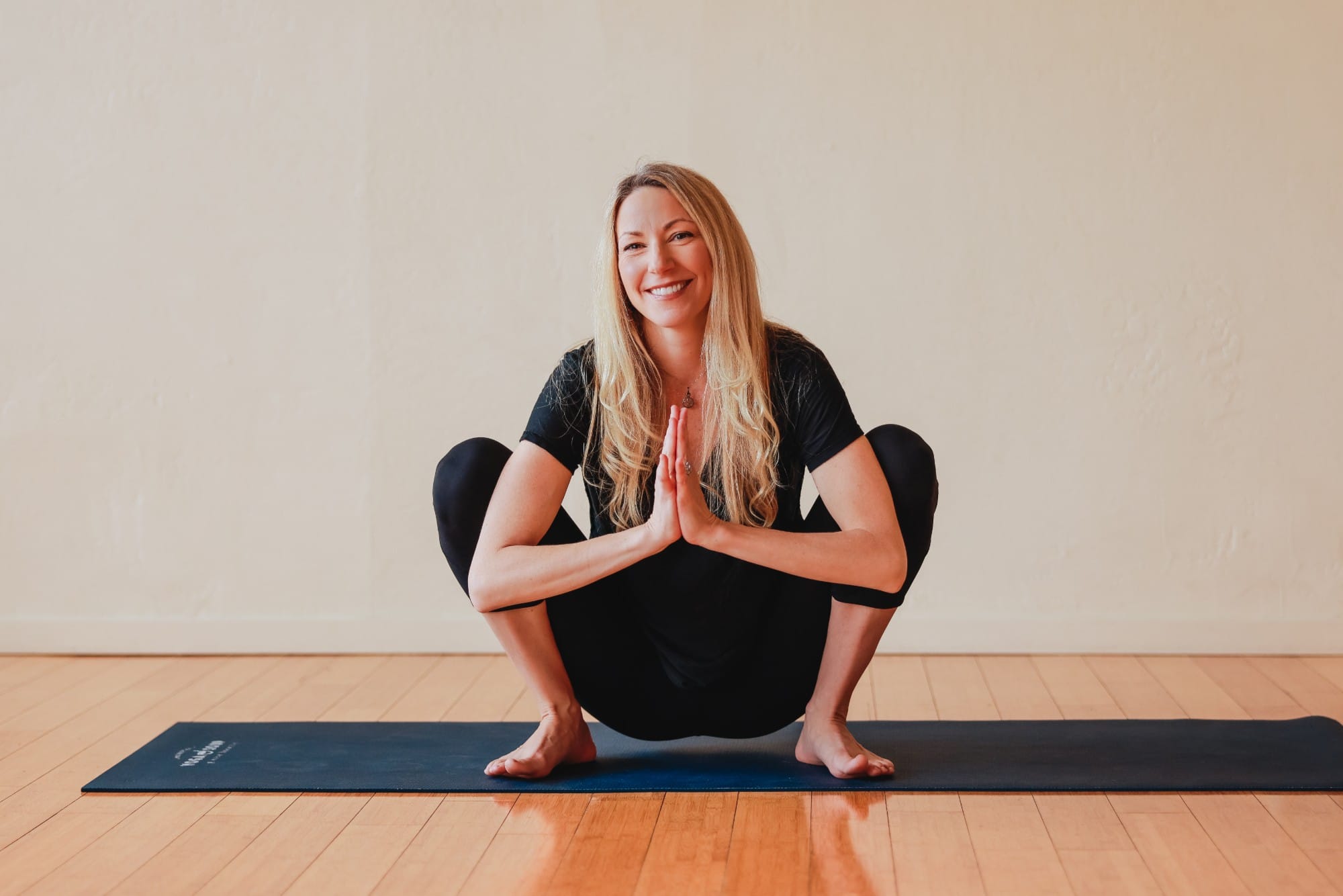Kara Goldstein smiling on her yoga mat, hands at her heart